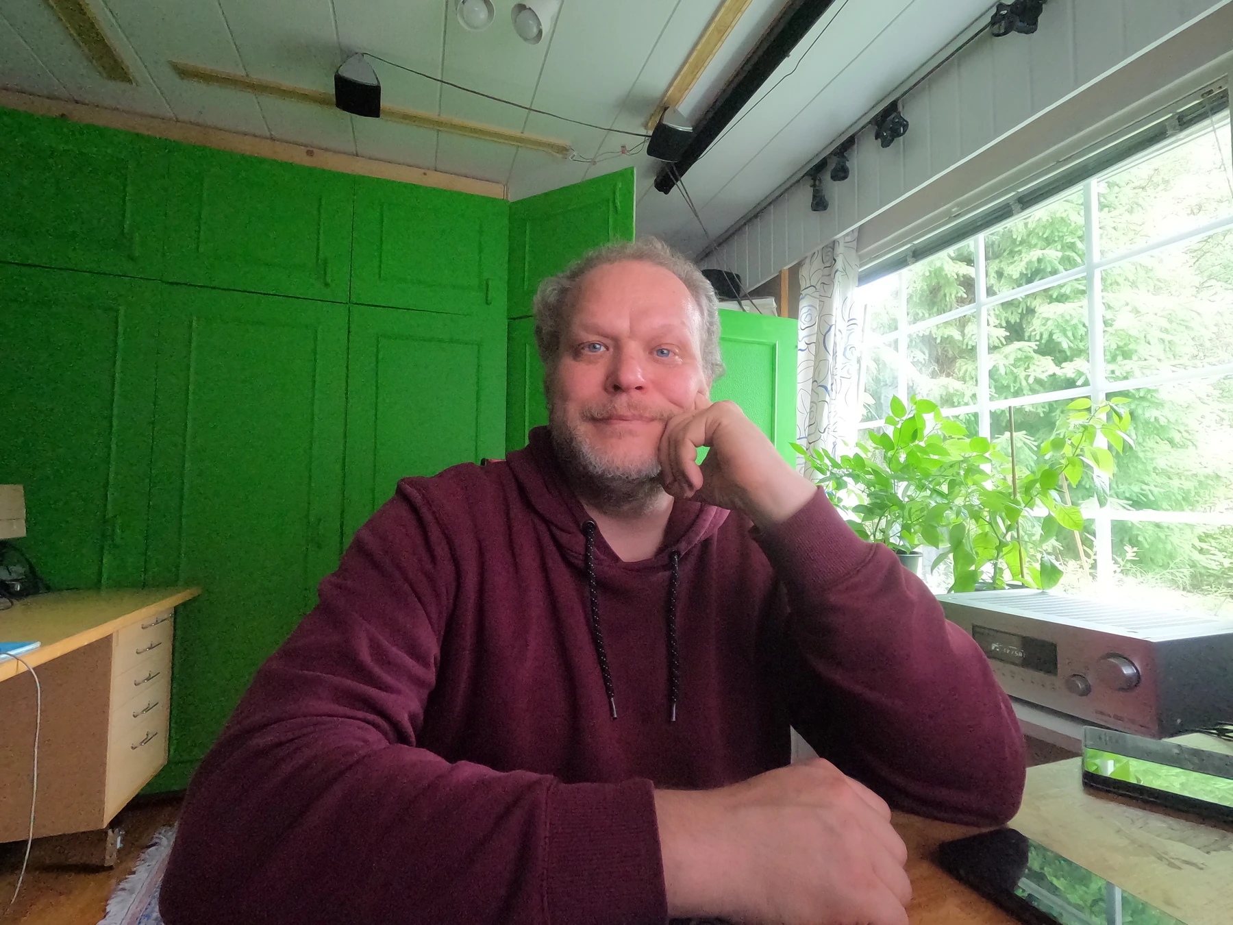 Kristian istuu työpöydän ääressä viininpunaisessa hupparissa, käsi poskella.