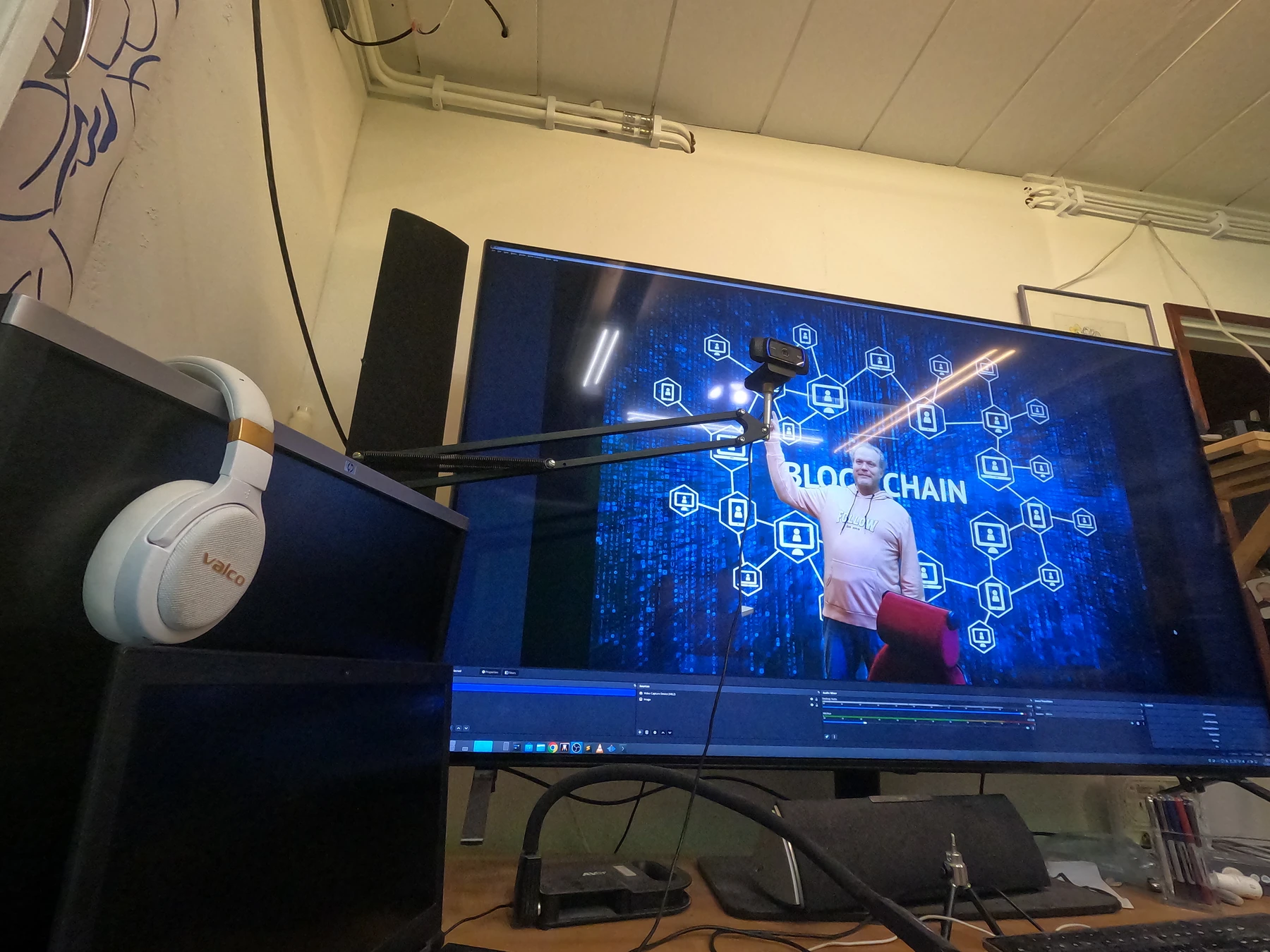 Työpisteessä on suureen näyttöön kiinnitetty kamera ja kuulokkeet; näytöllä näkyy Kristian videonäkymässä.